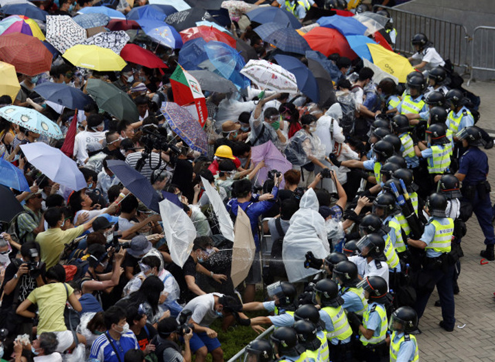 Protesters take cover from pepper spray with umbrellas as riot police clash with tens of thousands of protesters blocking the main street leading to the financial Central district outside the government headquarters in Hong Kong - Ziarul National